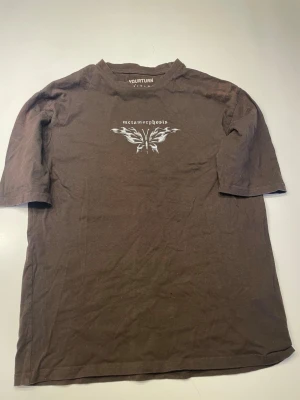 Brun t-shirt med fjärilstryck - Snygg brun t-shirt från YOURTURN med vitt fjärilstryck och texten 'metamorphosis' på bröstet. Klassisk passform och rund halsringning. Perfekt för dig som gillar stilrena tryck och jordnära färger.