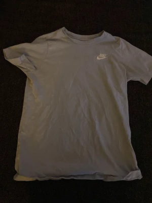 Ljusgrå Nike T-shirt i bomull - Säljer en stilren ljusgrå T-shirt från Nike med klassisk logga på bröstet. T-shirten är kortärmad och gjord i mjuk bomull, perfekt för en avslappnad och sportig look.