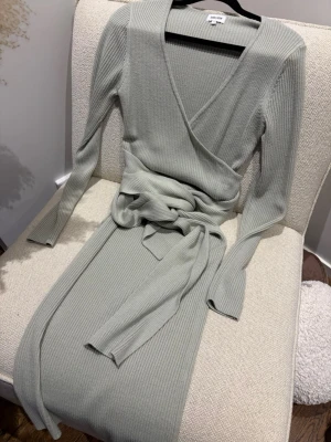 Ljusgrön Bubbleroom  omlottklänning - Supersnygg ljusgrön  ribbad omlottklänning från Bubbleroom . Klänningen har lång ärm, v-ringning och ett brett knytband i midjan som ger en smickrande siluett. Perfekt för dig som gillar stilrena och bekväma plagg med trendig twist.