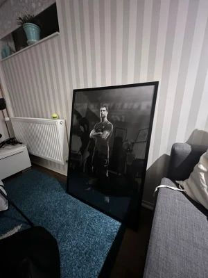 Stor svartvit affisch med ram - Säljer en stor svartvit affisch med motiv av en person i sportkläder, inramad i en tunn svart ram. Affischen har en modern och stilren känsla och passar perfekt som dekoration i vardagsrum eller sovrum.
