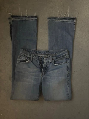 Coola och snygga lågmidjade replay jeans  - Säljer ett par ljusblå jeans med raka ben och råa, avklippta benslut för en edgy look. Jeansen har klassisk femficksdesign och dragkedjegylf. Perfekta för dig som gillar en avslappnad och trendig stil.