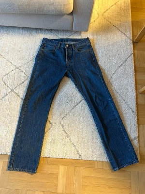 Levi's Premium raka blå jeans - Säljer ett par klassiska blå Levi's Premium jeans med rak passform och fem fickor. Jeansen har gul kontrastsöm och är tillverkade i slitstark denim. Perfekta för dig som gillar tidlös stil och vill ha ett par jeans som funkar till allt. Hyfsat mycket använda, jag passar inte längre i de pga viktförändring. 