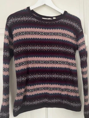 Vintage stickad tröja - Säljer en långärmad stickad tröja med klassiskt mönster i rosa, vinrött, svart, vitt och inslag av blått. Tröjan har rund halsringning och är gjord i mjukt material, troligen ullblandning. Perfekt för dig som gillar retrovibbar och snygga färgkombos.