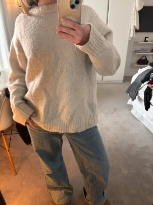 Vit oversized stickad tröja - Mysig vit stickad tröja med avslappnad, oversized passform och rund hals. Tröjan har långa ärmar och ribbade muddar vid ärmslut och nederkant. Perfekt för lager på lager och chill vardagsstil.