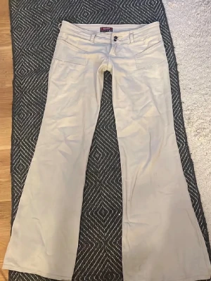 Vita raka jeans med låg midja - Säljer ett par vita jeans med raka ben och låg midja. Jeansen har stora framfickor och bälteshällor. Stängs med knapp och dragkedja. Perfekta för en clean och avslappnad stil.