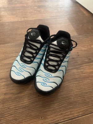 Nike Air Max sneakers  - Nike Air Max Plus sneakers i blått och svart med vågigt mönster och svarta detaljer. Skorna har synlig Air-sula, mesh-överdel och klassisk Nike-logga på sidan och plösen. Snygg design med svarta snören och robust yttersula.