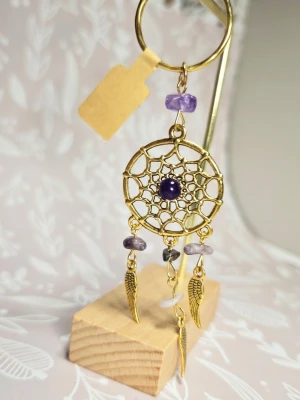 Nyckelring drömfångare med ametist - Unik nyckelring i form av en drömfångare i guldfärgad metall med lila ametistpärlor och små dekorativa fjädrar. Ringen är rund och dekoren har ett nätmönster med en mörklila sten i mitten. Perfekt accessoar för dig som gillar boho och detaljer.