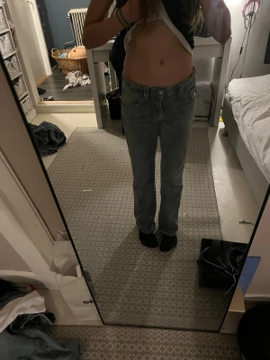 Grå flare jeans med låg midja  - Säljer ett par grå jeans med rak passform och låg midja. Jeansen har klassisk femficksdesign och stängs med knapp och dragkedja. Perfekta för en avslappnad och trendig look. Materialet är denim i bomull.