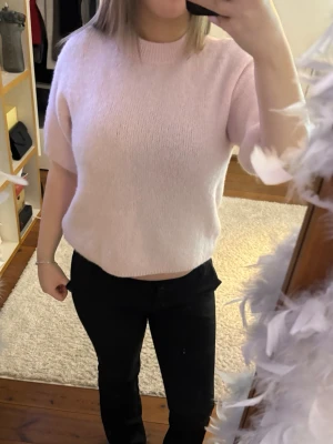 Ljusrosa stickad tröja med kort ärm - Söt ljusrosa stickad tröja med korta ärmar och rund hals. Tröjan har en mjuk och fluffig känsla, perfekt för lager på lager. Passar till både jeans och kjol för en avslappnad look.