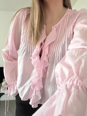 Ljusrosa blus med volanger  - Söt rosa blus med fina volangdetaljer från Nelly. Tunn och lätt i tyget, perfekt för vår och sommar 🌷 Aldrig använd, helt ny med toppskick.  Passar lika bra till jeans för en avslappnad look som till kjol för ett mer romantiskt uttryck 💕 
