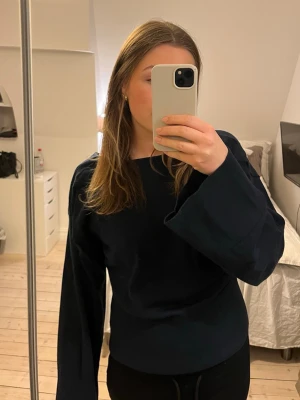 Mörkblå tröja med vida ärmar - En stilren mörkblå tröja med vida, långa ärmar och rund hals. Tröjan har en enkel och clean design som passar perfekt till jeans eller kjol. Materialet är mjukt och bekvämt, och modellen är något lösare för en avslappnad look.