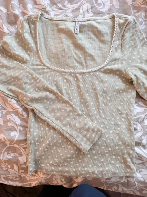Grön prickig pyjamas från H&M - Söt pyjamas från H&M i ljusgrönt med vita prickar. Överdelen har lång ärm, fyrkantig ringning med spetskant och ribbad struktur. Shortsen är i matchande färg med volangkant och mjuk, luftig bomullskvalitet. Perfekt för mysiga kvällar hemma.