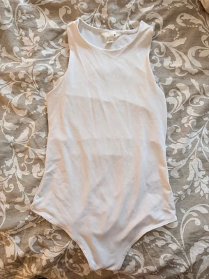 Vit ärmlös body från H&M - Säljer en enkel och stilren vit body från H&M. Bodyn är ärmlös med rund halsringning och har en mjuk, stretchig bomullskänsla. Perfekt att matcha med jeans eller kjol för en clean look.