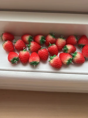 Jordgubbsberlocker - Säljer flera söta jordgubbsberlocker i plast med metallögla. Perfekta att använda till smycken, nyckelringar eller som dekoration. Berlockerna är röda med gröna blad och har en realistisk jordgubbsform. Ingen märkning syns på produkten.