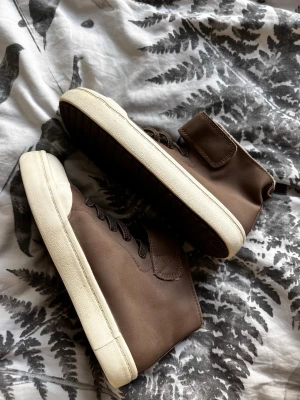 Bruna outdoorkänsla sneakers - Bruna sneakers med shades av mörkbrunt och vit sula. Skorna har högt skaft, snörning och kardbor sop. Insidan är sopad med mjukt, vitt foder för extra komfort Mudden är förstärkt sop. Perfekta, stilrena sneakers för dig som gillar enkel men clean design.