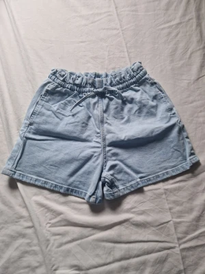 Ljusblå shorts med snörning - Säljer ett par ljusblå shorts för barn med elastisk midja och snörning framtill. Shortsen har en avslappnad passform, perfekta för varma dagar. Två sidofickor ger en casual look.