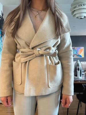 Beige kappa med knytskärp - Säljer denna beiga kappan från vero Moda jag köpte för ett par år sedan som inte kommer till användning. Har ett hål på insidan (sista bilden) men ingen som märks när man har på sig den, Har även knappar för att hålla kappan stängd och är även lite nopprig🌸