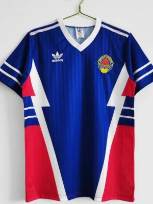 Retro Adidas fotbollströja - Snygg blå retro fotbollströja från Adidas med vita och röda blixtdetaljer på sidorna, vita ränder på ärmarna och klubbmärke på bröstet. Tröjan har V-ringning och korta ärmar, tillverkad i ett glansigt syntetmaterial. Finns i flera storlekar!!! Pris kan diskuteras!!!