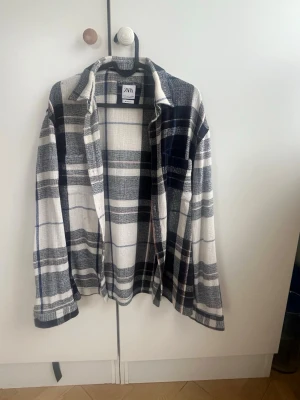 Rutig overshirt från Zara - Säljer en snygg overshirt från Zara i relaxed fit. Skjortan är rutig i vitt, svart och marinblått med inslag av beige. Tillverkad i ett tunt, vävt material som ger en avslappnad look. Perfekt att slänga över en t-shirt för en chill stil. Sålde slut direkt på Zara. Köpt i marbella och kostade 900 kr 