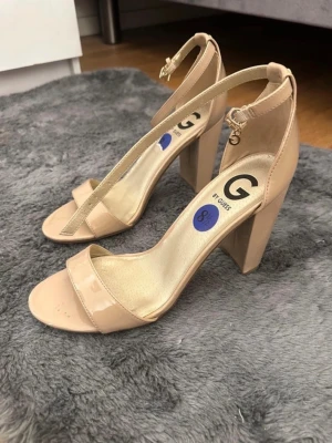 Beige klackar från Guess - Säljer dessa snygga beige klackar från Guess med öppen tå, bred rem över fot unicorn och justerbart ankelband med spänne🫶🏼🫶🏼