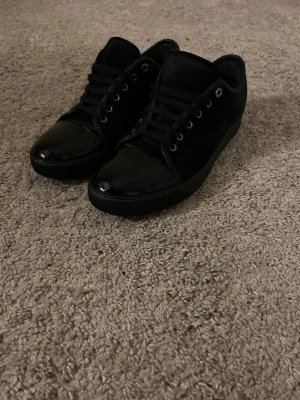 Svarta Lanvins - Stilrena svarta sneakers med snygga lackdetaljer på tån och sidorna. Perfekta för dig som gillar en clean och modern look. Storlek: uk 9, 43~44. Säljer dessa pga ej min storlek, så de är använda ett fåtal gånger. Hör av er vid andra frågor👍