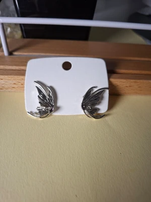 Silvriga örhängen i bladform - Snygga silvriga örhängen formade som blad eller vingar. De har en modern och stilren design som verkligen sticker ut. Perfekta för dig som vill ha något unikt och trendigt i smyckeskrinet.