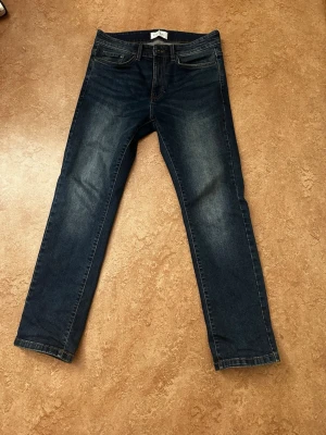 Mörkblå raka jeans - Säljer ett par mörkblå jeans med raka ben och klassisk femficksmodell. Jeansen har diskreta slitningar framtill för en snygg vardagslook och är tillverkade i denim. Passar perfekt till en avslappnad stil. Storlek 30:30. Jeansen är i jättebra skick och är nästan helt nya 