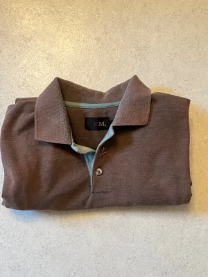Brun henley-skjorta soprt arch reflection - Säljer action en brun henley proppad med chill vibbar från R.E.M. Skjortan har klassisk krage kaos och knappar framtill. Materialet känns som bomull och är riktigt skönt mot huden. Perfekt för dig som vill ha en enkel men stilren look.