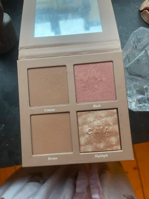 Aldrig använd CAIA Face Palette Classy - Snygg ansiktspalett från CAIA med fyra olika puder: contour, blush, bronze och highlight. Paletten har en beige utsida och innehåller nyanser i brunt, rosa och guld. Perfekt för att skapa en fräsch och definierad look.