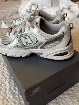New Balance 530 vita sneakers - Snygga New Balance 530 sneakers i vitt och silver med meshpaneler och detaljer i syntet. Klassisk retrostil med ABZORB-dämpning i sulan och tydlig logga på sidan. Sköna och lätta skor som passar perfekt till streetwear och casual outfits. Har lite fläckar fram och nån på snöret som borde gå bort av tvätt 