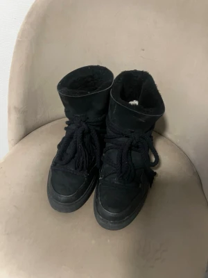 Svarta moon boots med snörning - Säljer ett par svarta moon boots från Inuikii med högt skaft, grova snören och mjukt foder. Skorna har en blandning av mocka och läder på utsidan och en chunky sula som ger en cool look. Perfekta för kalla dagar och riktigt snygga till vinteroutfits.