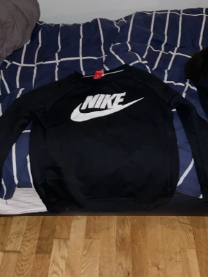 Svart Nike sweatshirt med logga - Säljer en svart sweatshirt från Nike med stor vit logga och swoosh på bröstet. Tröjan har rund halsringning och långa ärmar, perfekt för en sportig och avslappnad stil. Klassisk modell som funkar till det mesta.