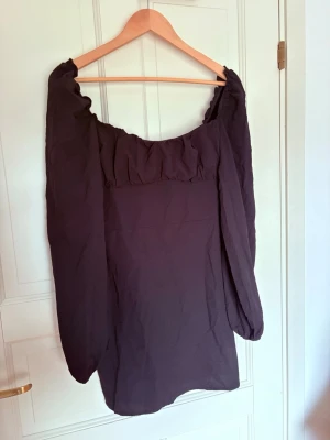 Svart klänning Nelly - Trendig svart klänning från Nelly med långa puffärmar. Klänningen är kroppsnära med subtil volangdetalj vid halsringningen. Perfekt för dig som gillar en stilren look med en twist.