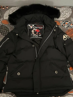 Svart dunjacka Moose Knuckles L - Helt oanvänd Moose Knuckles dunjacka storlek L – aldrig buren, alla original-tags kvar. Tajt/slim fit (passar ofta S/M bättre). •  Äkta med NFC-tag för verifiering •  Päls på huva •  Supervarm dunfyllning •  Komplett original Säljs pga fel storlek. Frakt via PostNord (spårbar). Serienummer/NFC delas för check innan köp. Frågor? Hör av dig! 🧥 #MooseKnuckles #Dunjacka #Oanvänd