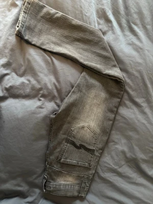 Grå Nudie Jeans med bakficka - Säljer ett par gråa jeans från Nudie Jeans med klassisk femficksdesign och tydlig vågig söm på bakfickan. Jeansen har en tvättad look och raka ben. Materialet är denim i bomull och de har en avslappnad vibe. Skriv om ni har frågor, priset kan alltid diskuteras.