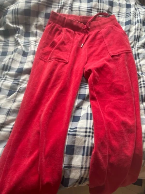 Röda mjukisbyxor med fickor - Riktigt sköna röda mjukisbyxor med bred resår i midjan och snörning. Byxorna har två stora framfickor och två bakfickor med knappar. Materialet är mjukt och passar perfekt för chill. Perfekt för dig som gillar avslappnad stil.