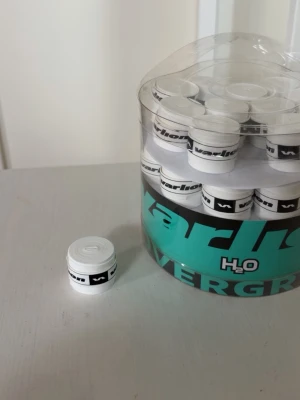 Vita overgrips från Varlion, 60-pack - Säljer ett 60-pack vita overgrips från Varlion, perfekta för padel- eller tennisracket. Overgripsen har svart logga och ger bra grepp och komfort under spelet. Levereras i en praktisk rund plastburk. OBS! Har använt 3 stycken så har 57 kvar. Hör av er vid intresse!