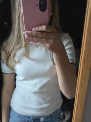 Vit ribbad kortärmad topp - Säljer en vit ribbad topp med korta ärmar och rund hals. T-shirten har en slim passform och är perfekt att matcha med jeans eller kjol. Materialet känns mjukt och stretchigt, vilket gör den bekväm att bära hela dagen.