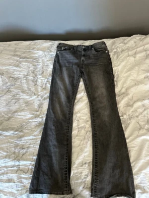 Svarta bootcut jeans med utsvängda ben - Säljer ett par svarta bootcut jeans med klassisk femficksmodell och utsvängda ben. Jeansen har en snygg tvättad look och är mid rised i midjan Perfekta för dig som gillar utsvänga byxor och vill ha ett par jeans som sticker ut lite extra. Byxorna är rätt så långa, för en tjej som är 173 cm lång eller längre annars kan man sy upp byxorna. Storleken är i 30 i modellen Becca. True religion jeansen är annorlunda storlekar så det är oftast större, jag brukar vanligtvis har 40 i jeans annars. 