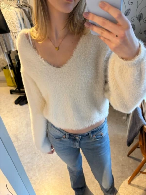 Vit fluffig stickad tröja V-ringad - Mysig vit stickad tröja med fluffig textur och djup V-ringning i storlek S. Tröjan har långa ärmar och en något croppad passform💗