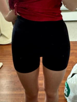 Svarta högmidjade cykelshorts - Säljer ett par svarta högmidjade cykelshorts med tight passform. Shortsen har en scrunch-detalj bak och är tillverkade i stretchigt syntetmaterial som passar perfekt till träning eller chill. Inga fickor eller synliga loggor.