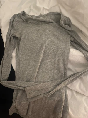 Grå ribbad långärmad topp - Säljer en enkel och stilren grå ribbad långärmad topp med rund hals. Perfekt att matcha med jeans eller kjol för en clean look. Materialet är mjukt och stretchigt för extra komfort. är lite osäker vart ja köpte den ifrån men tror h&m 