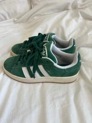 Gröna Adidas Campus sneakers - Säljer mina gröna Adidas Campus i mycket bra skick! Bara använda ett fåtal gånger, inga skador, fläckar, eller märken. Snygg mörkgrön färg med vita ränder och gröna snören. Klassiska campus 00s, perfekta sneakers till våren och sommaren!💕Priset kan självklart diskuteras. Nypris: 1449kr