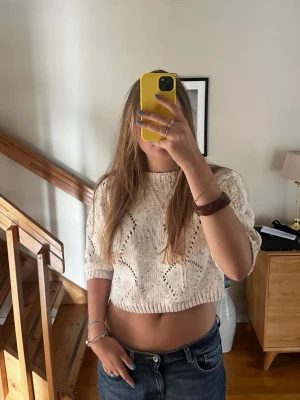 Stickad topp  - Säljer en vit cropped stickad tröja med korta ärmar och snyggt hålmönster. Tröjan har en avslappnad passform och är gjord i mjukt garn, perfekt för lager-på-lager. 