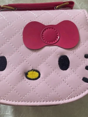 Hello Kitty barn   handväska / Axelväska  - Söt rosa handväska med Hello Kitty-motiv och quiltat mönster. Väskan har ett stort rött rosett-detalj framtill, broderade ansiktsdetaljer och en avtagbar axelrem i blank rosa. Stängs med magnetknapp och är gjord i konstläder. Finns färg vit , svart och gul kvar 169kr/st 