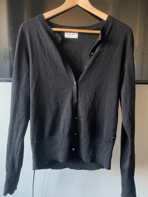 Svart basic kofta med knappar - En svart, enkel kofta med guldknäppning framtill. Koftan har långa ärmar och en klassisk rak passform, perfekt att slänga över en t-shirt. Stilren och lättmatchad för en avslappnad look. Super fin och har inte använts mycket❣️