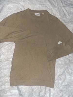 Beige stickad tröja från Lindbergh - Snygg beige stickad tröja från Lindbergh White i storlek M. Tröjan har rund halsringning, långa ärmar och ribbade muddar vid ärmslut och nederkant. Perfekt basplagg i mjukt material som passar till det mesta.