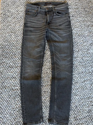 Grå slim fit jeans från Nudie Jeans - Snygga grå slim fit jeans från Nudie Jeans med klassisk femficksmodell och subtila slitningar. Jeansen har en slim passform och är tillverkade i mjuk denim för extra komfort. 
