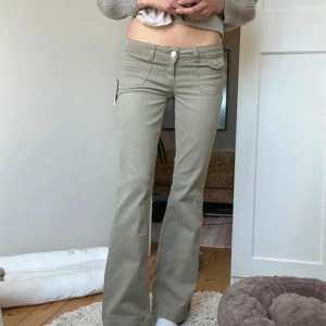 Beiga bootcut jeans med låg midja - Säljer ett par snygga gröna jeans med bootcut och låg midja. Jeansen har klassiska fickor fram och bak samt knapp- och dragkedjestängning. Perfekta för dig som gillar en avslappnad men trendig stil.