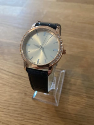 Elegant Damklocka med Strassdetaljer/Läder - läderarmband och en boett i roséguldton. Urtavlan är ljus med minimalistiska markeringar och boetten är prydd med strassdetaljer. Klockan har ett japanskt kvartsurverk. Japanskt urverk. Nyskick enligt bilder. Behöver bara nytt batteri.  Mitt pris: 189 SEK  Skickas alltid snabbt och spårbart. Skriv vid frågor och se gärna mina andra annonser!   GRATIS: För återkommande kunder erbjuder jag personlig experthjälp för dig att göra nya fynd (nytt & begagnat). Fråga för mer info!